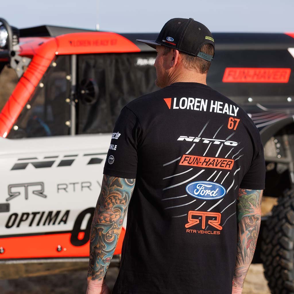 Loren Healy wearing his 2025 RTR Vehicles Off-Road Team Shirt, featuring motorsport-inspired design, stands beside his Ultra4 race truck