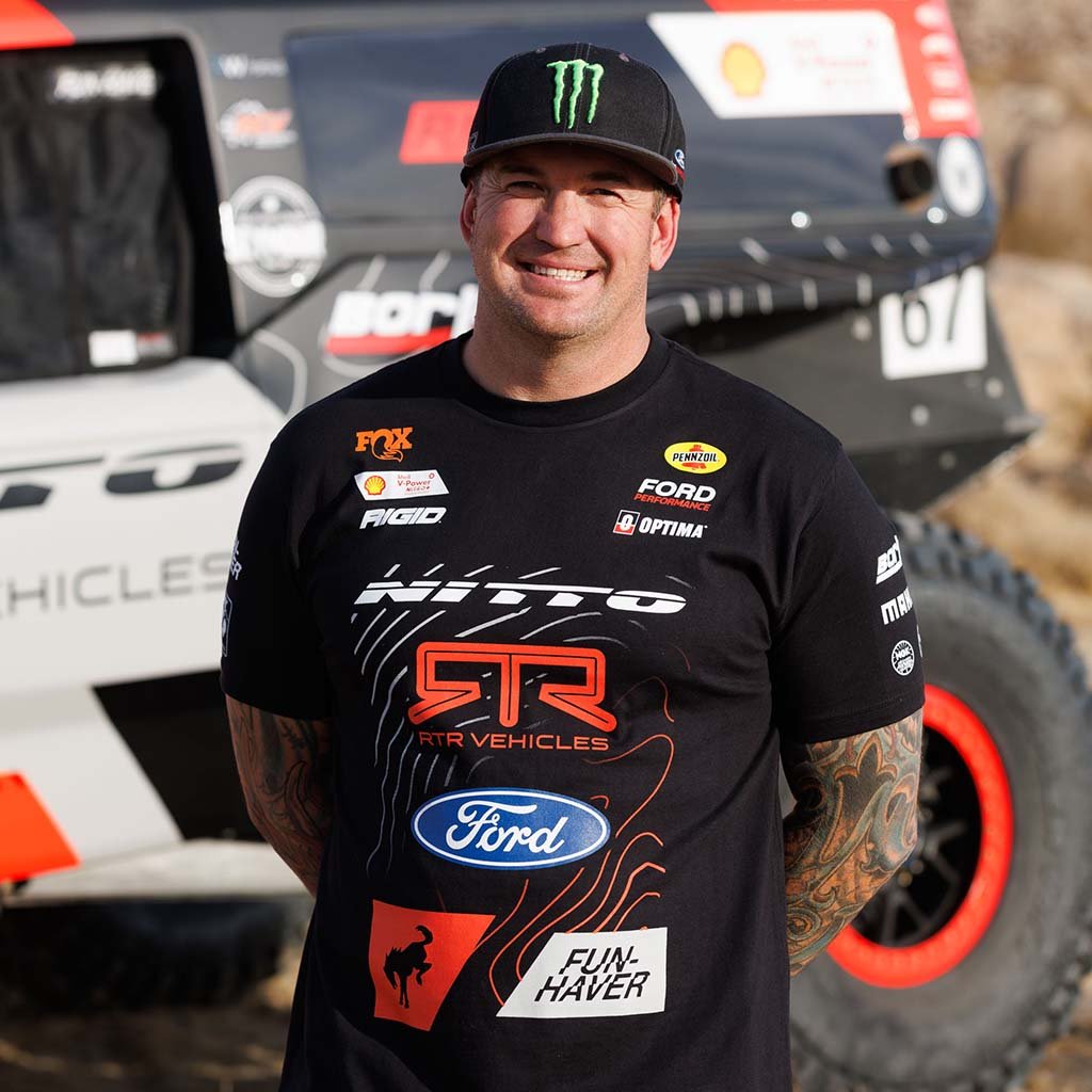 Loren Healy wearing his 2025 RTR Vehicles Off-Road Team Shirt, standing by a Ultra4 4400 truck, showcasing the shirt's design with off-road motorsports themes