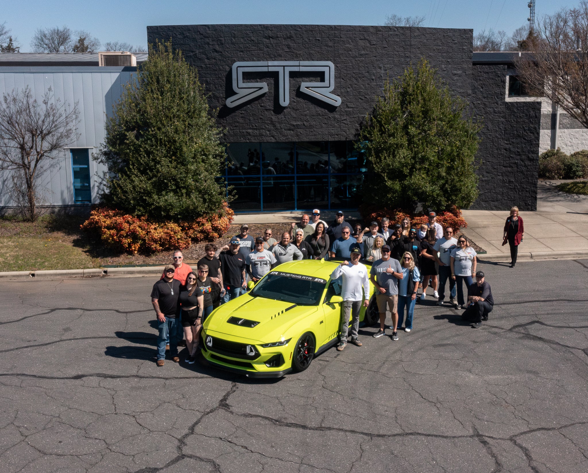 Vaughn Gittin Jr and RTR Owners pose for a picture in front of the RTR Lab with a Hyper Lime Mustang RTR