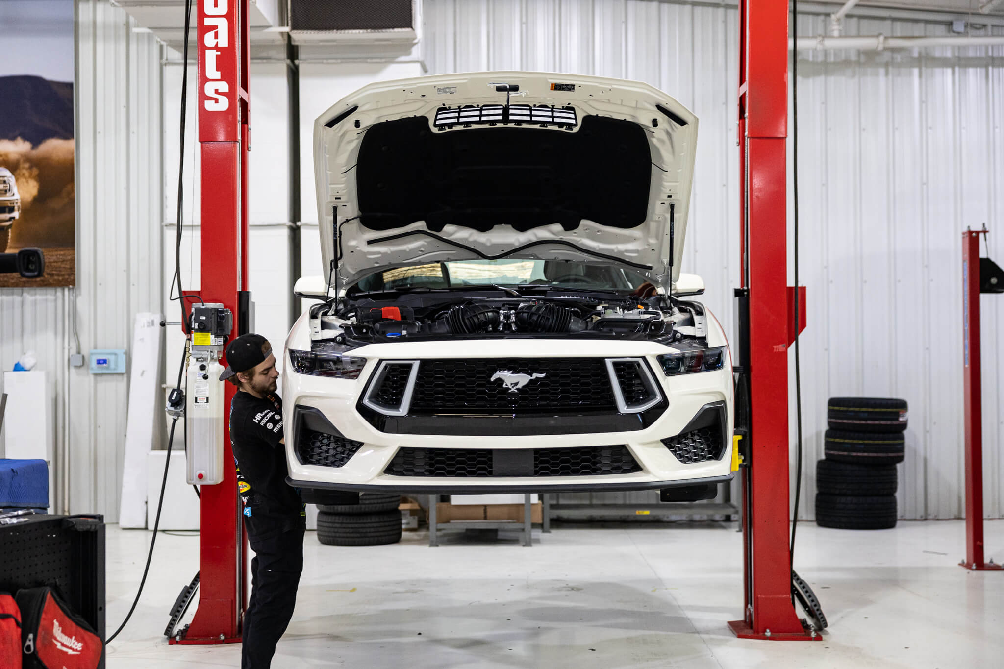 A man is working on a 2025 Wimbledon white 60th anniversary Mustang on a car lift