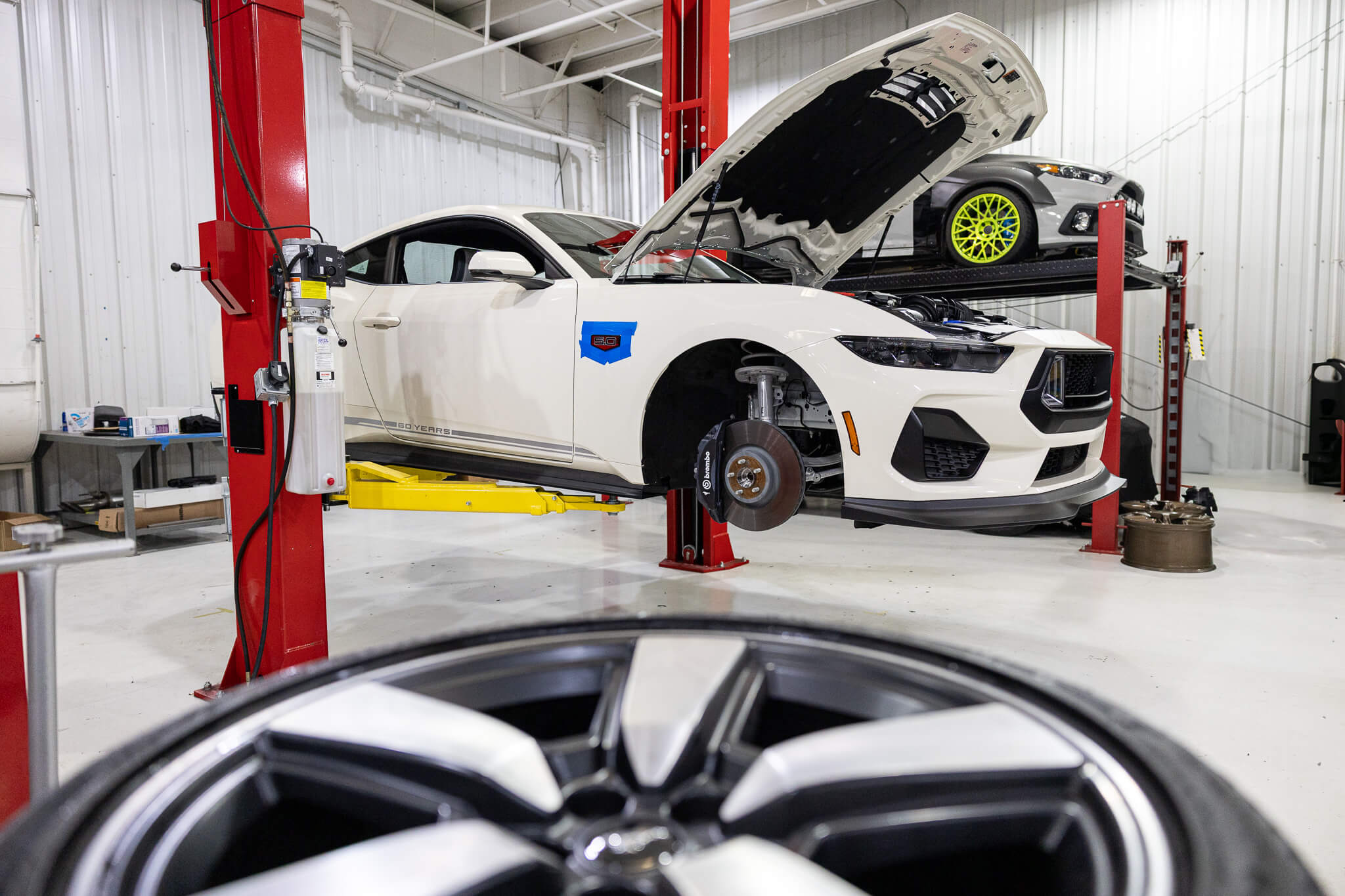 A Wimbledon white 60th anniversary Mustang on a car lift being built into a Mustang RTR in front of a set of wheels