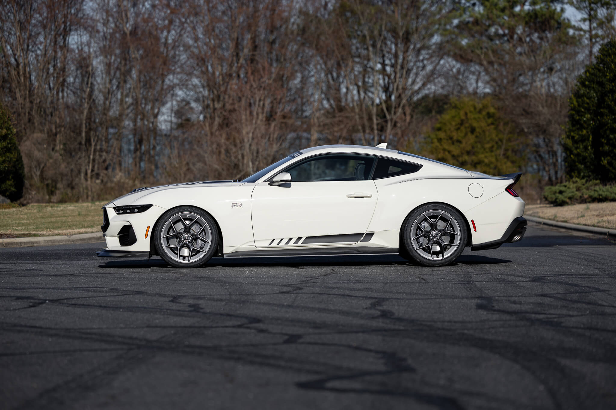 A side profile of a 2025 Wimbledon white 60th anniversary Mustang RTR on an asphalt road