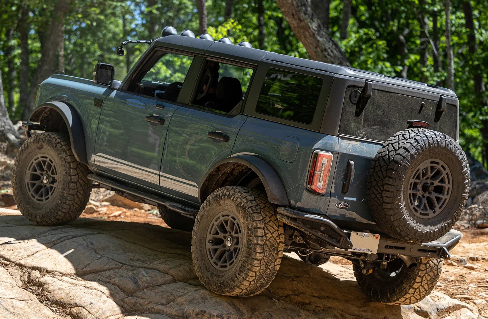 Bronco Trail Safe Package for 21+ Bronco on rocky hill, highlighting rugged tires, rock sliders, and bumper end caps for enhanced off-road performance and style.